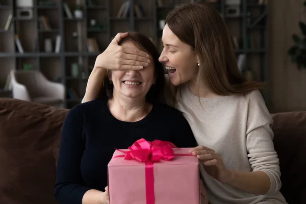 Kärleksfull vuxen dotter nära pensionerad mor ögon gör närvarande överraskning — Stockfoto