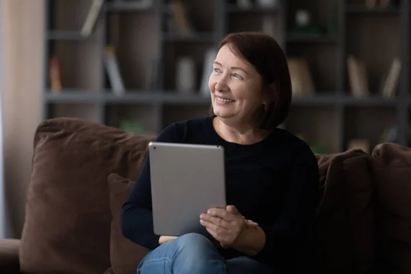 Femme âgée se détendre sur le canapé avec tablette électronique regarder de côté — Photo