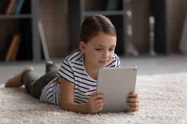 Mutlu ergen kız çocuğu dijital dokunmatik ped kullanarak halıda yatıyor.