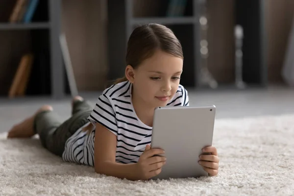 Happy tween girl child lying on carpet using digital touchpad — 图库照片