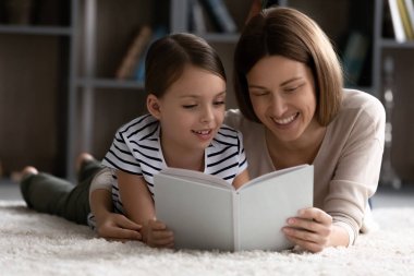 Genç anne ve küçük kızı halının üzerinde rahatlayıp kitap okuyorlar.