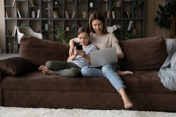 Millennial trabalho mãe no laptop abraço tween criança usando telefone — Fotografia de Stock