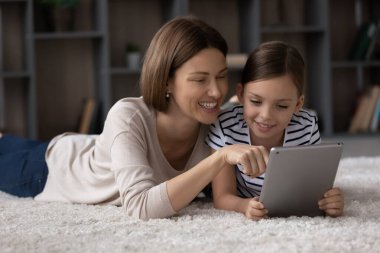 Gülümseyen bekar anne, reşit olmayan kızına tablette fotoğraf gösteriyor.