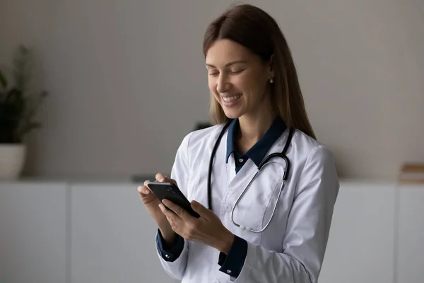 Улыбающаяся юная леди доктор держит телефон сделать звонок пациенту — стоковое фото