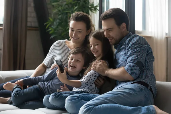Happy young parents with kids using smartphone at home together — Stock Photo, Image