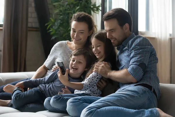 Joyeux jeunes parents avec des enfants utilisant un smartphone à la maison ensemble — Photo