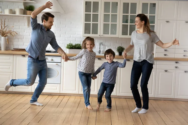 Щаслива сім'я з двома дітьми танцює на сучасній кухні разом — стокове фото