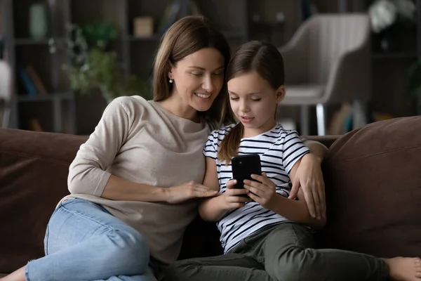 Geïnteresseerde moeder kijken tussen dochter spelen spel op moderne smartphone — Stockfoto