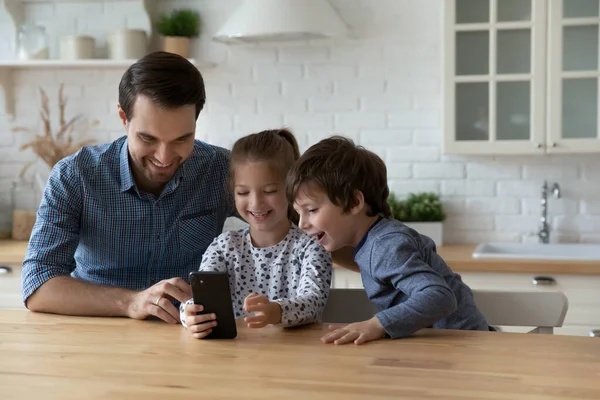 Lächelnder Vater mit zwei Kindern, die zu Hause gemeinsam telefonieren — Stockfoto