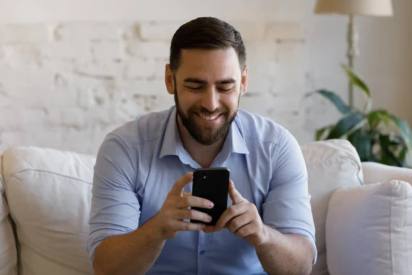 Happy millennial knappe man met behulp van mobiele telefoon toepassingen thuis. — Stockfoto