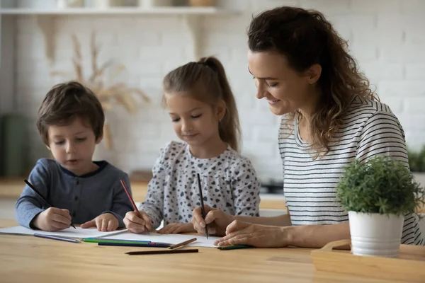 Lächelnde fürsorgliche Mutter und kleine Kinder zeichnen mit bunten Bleistiften — Stockfoto