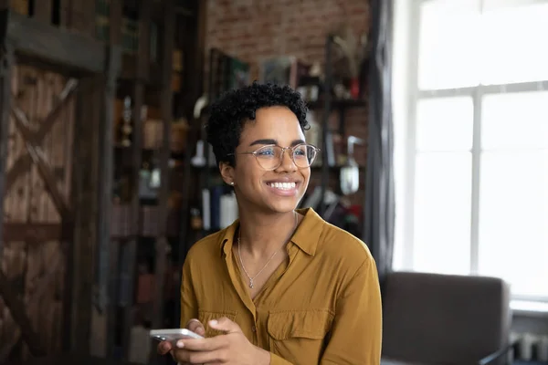 Glückliche junge Afroamerikanerin mit Handy blickt in die Ferne. — Stockfoto