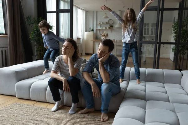 Laute Tochter und Sohn springen, müde Eltern sitzen auf der Couch — Stockfoto