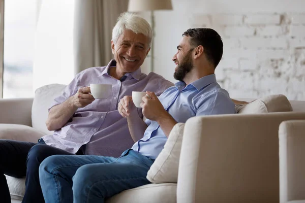 Szczęśliwe dwa pokolenia rodziny bawiące się rozmawianiem, piciem kawy. — Zdjęcie stockowe