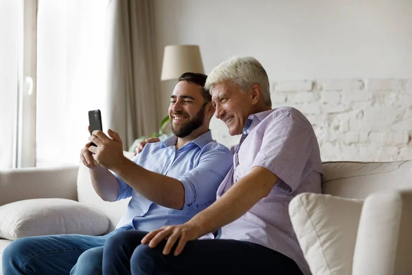 Счастливые два поколения мужчин семьи с помощью мобильных телефонов. — стоковое фото