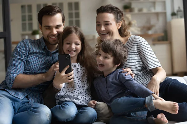 Mutlu ebeveynler ve iki çocuk akıllı telefonla eğleniyor. — Stok fotoğraf