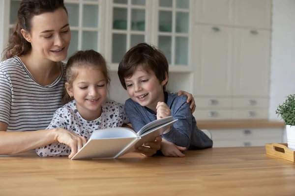 Любляча кавказька мати з дітьми вдома, які читають книжку — стокове фото