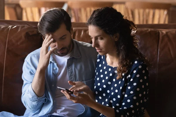 Confundida pareja familiar joven mirando la pantalla del teléfono inteligente. — Foto de Stock