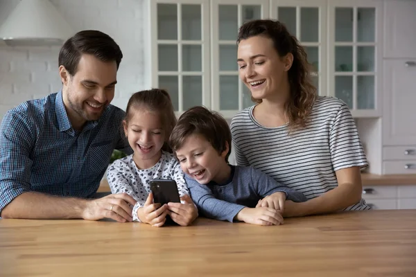 Padres felices con dos hijos usando smartphone en casa juntos — Foto de Stock