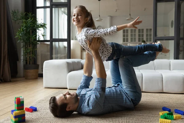 Happy father lying on floor, lifting excited daughter, having fun — 图库照片