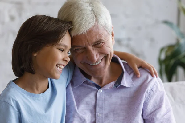 Happy preteen kid cuddling old grandfather at home. — Stock Photo, Image