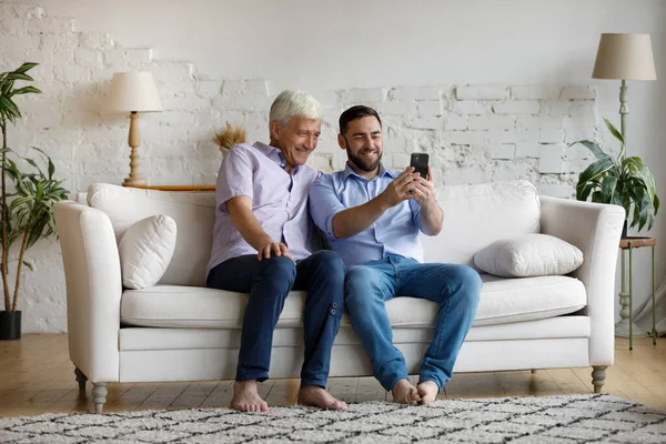 Joven feliz usando el teléfono celular con el padre mayor. — Foto de Stock