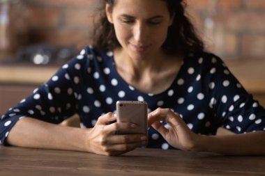 Gülümseyen Latin kadın akıllı telefon kullanıyor, masada oturuyor..