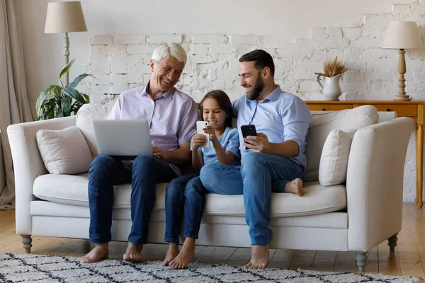 Heureuse famille multigénérationnelle détendue utilisant différents gadgets. — Photo