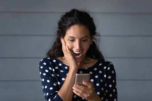 Счастливая удивленная молодая латиноамериканка смотрит на экран телефона. — стоковое фото