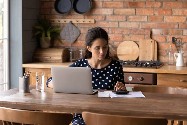 Geconcentreerde jonge Spaanse vrouw die de binnenlandse uitgaven berekent. — Stockfoto