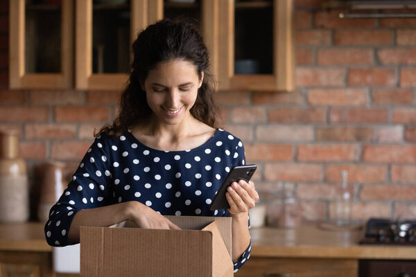 Smiling millennial hispanic woman unpacking parcel indoors.