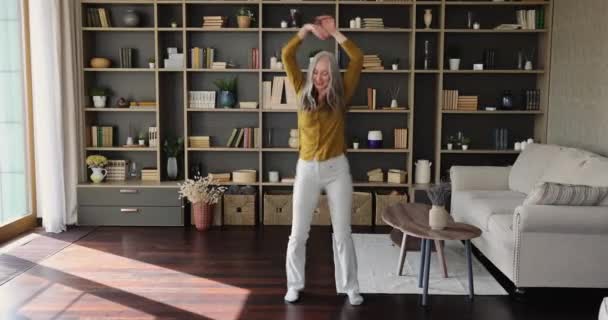 대담하게 날씬 한 여성 연금 생활자 가 거실에서 재미를 보면서 춤을 추는 모습 — 비디오