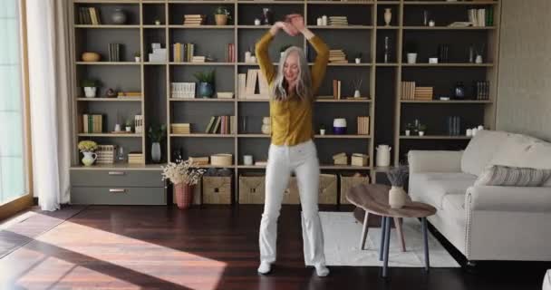 Energetic slim female pensioner dancing having fun at living room — Stockvideo