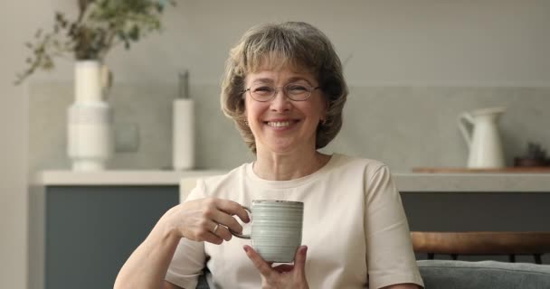 Happy senior woman posing at kitchen holding cup of tea — Stockvideo