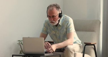 Kablosuz kulaklık çalışması yapan yaşlı bir erkek laptopun mesafesinde.