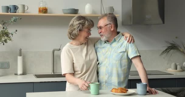 Affectionate aged married couple cuddle talk drink coffee with bakery — Stockvideo
