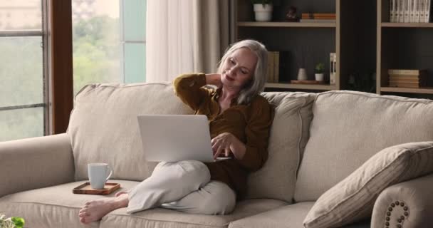 Ευχάριστη ηλικιωμένη κυρία απολαμβάνει ζεστό καφέ χρησιμοποιώντας υπολογιστή στο σπίτι — Αρχείο Βίντεο