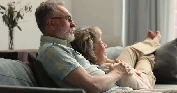 Loving aged husband hug shoulders of wife relaxing on sofa — Stockvideo