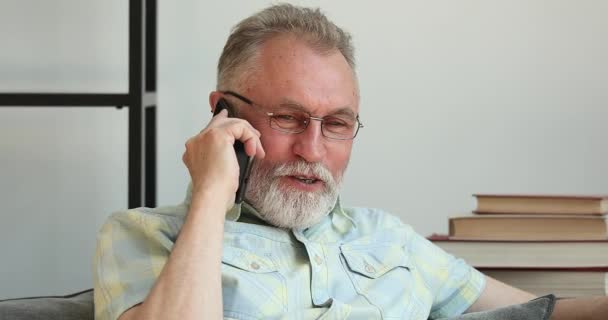 Улыбающийся пожилой мужчина в очках разговаривает по телефону — стоковое видео