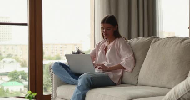 女性座っていますソファにホームタイピングでラップトップキーボード — ストック動画