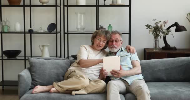 上了年纪的夫妻用平板电脑在沙发上聊天放松一下 — 图库视频影像