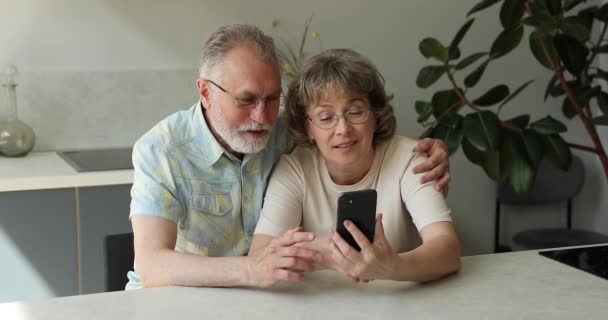 Amichevole nonni anziani abbracciare in cucina Guarda il video sul telefono — Video Stock