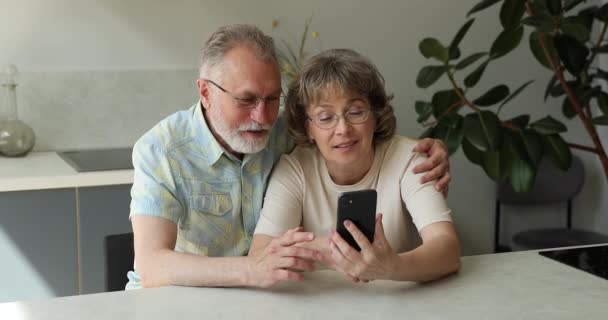 Amigável avós seniores abraçar na cozinha assistir vídeo no telefone — Vídeo de Stock