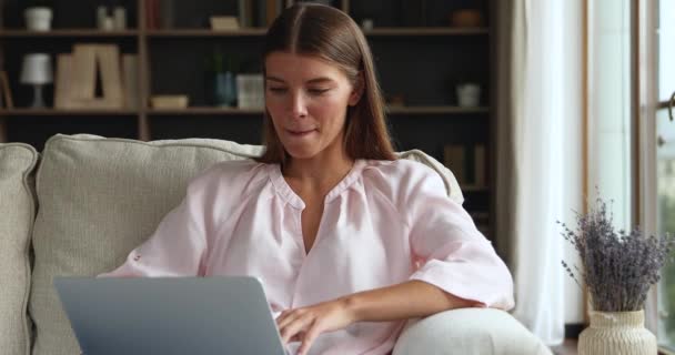 Красива молода жінка сидить на зручному дивані з ноутбуком — стокове відео