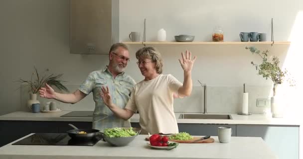 Active aged spouses pensioners dancing funny dances at home kitchen — Stock Video