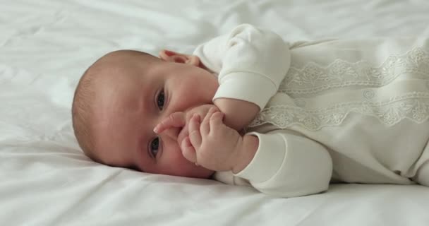 Cute baby wear sleepsuit lie on bed suckle fingers — Stock Video