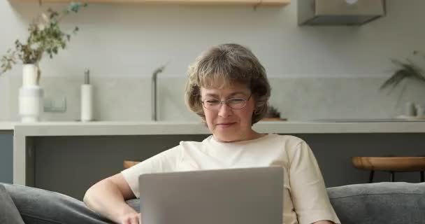 Радостная пожилая женщина общается с семьей по видеосвязи на ноутбуке — стоковое видео