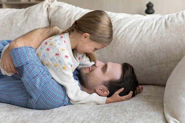 Smiling father talking with kid, lying on sofa. — Stock Fotó