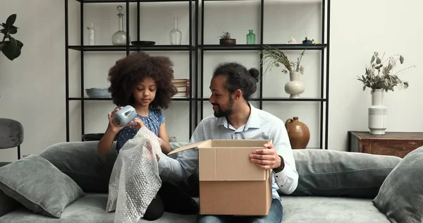 Cute African girl her dad unpack parcel box with kitchenware — Foto Stock