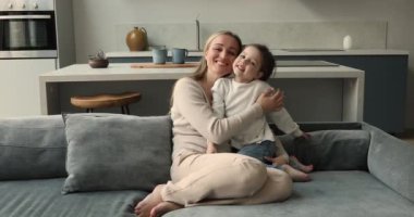 Kadın kızına sarılıyor kanepeye oturuyor ve kameraya bakıyor.